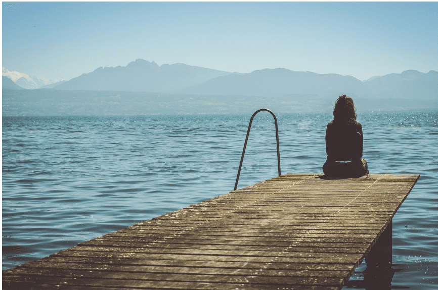 Frau, die auf einem Steg sitzt und auf den See guckt